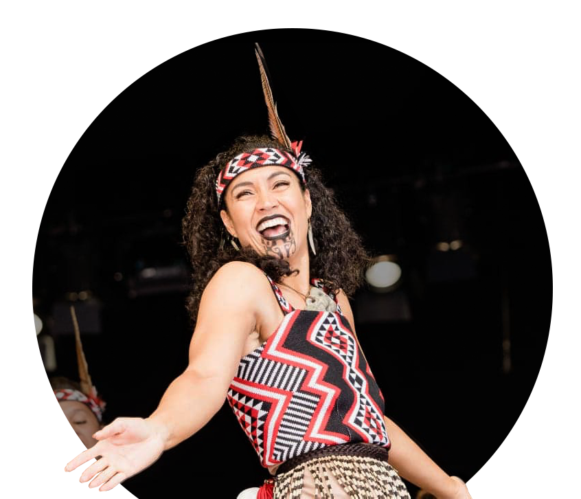A happy wahine performs Kapa Haka on stage, adorned in a custom-knitted kākahu made by Kapa Haka Makers Aotearoa.